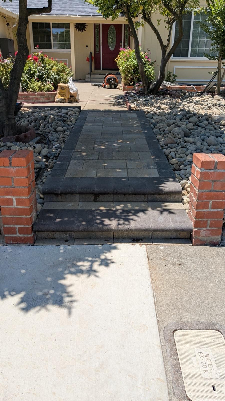 Paver walkway with charcoal border and steps leading to a front entry between brick pillars