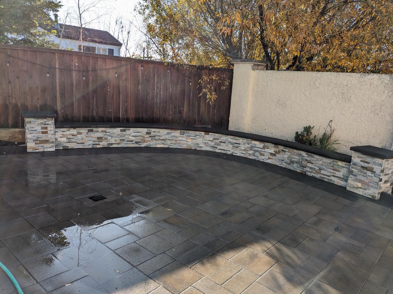 Curved stone veneer seating wall with pillar caps around a gray paver patio