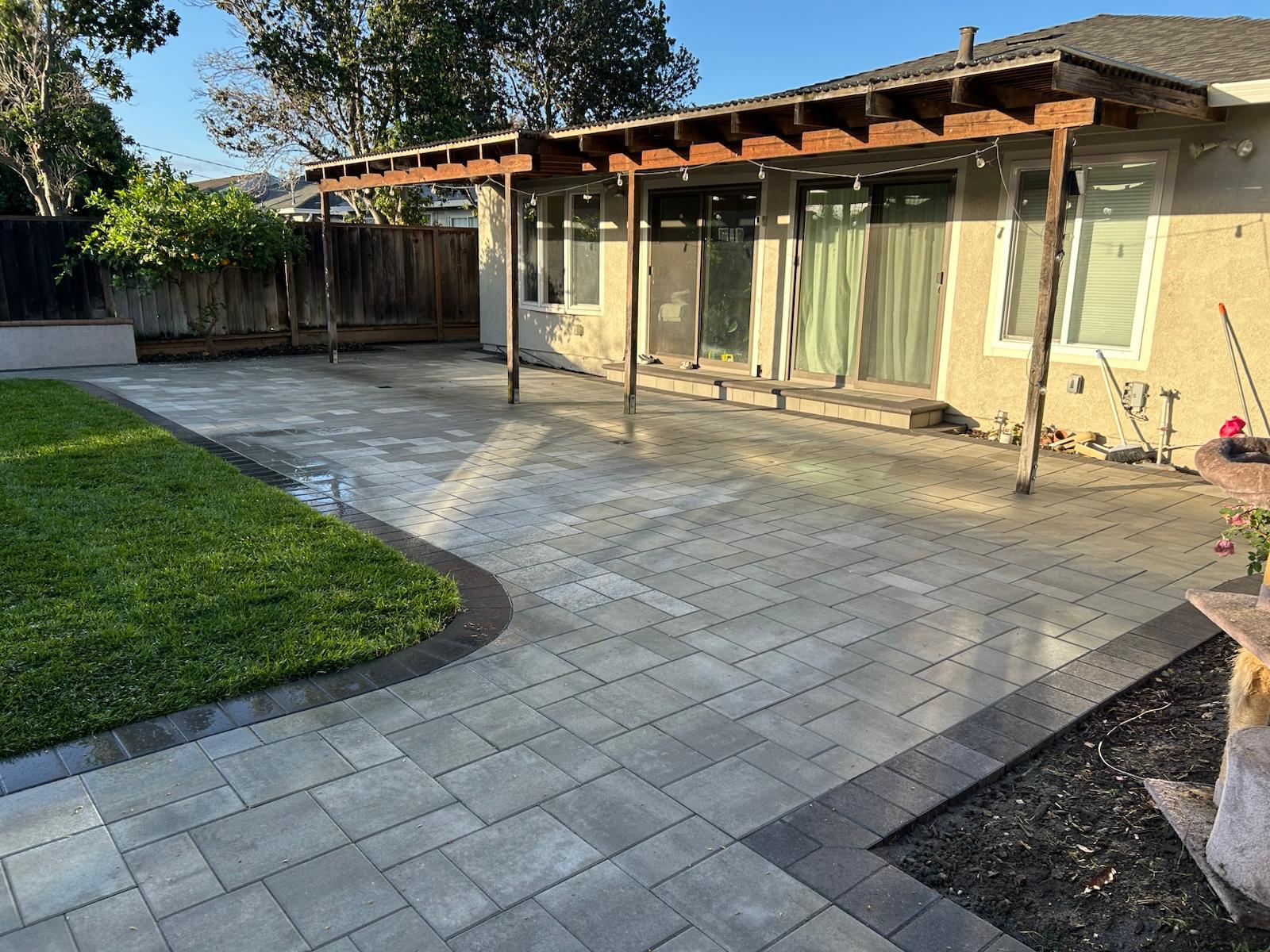 Large gray paver patio with charcoal border beside a green lawn under a covered patio