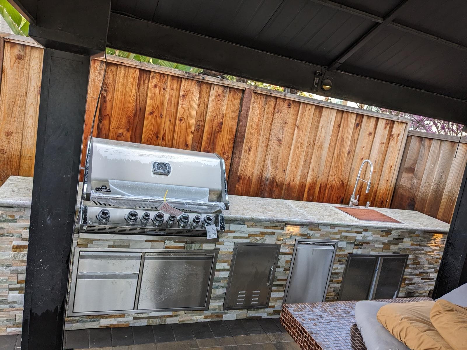 Covered outdoor kitchen with stacked stone base, built-in grill, sink and stainless storage