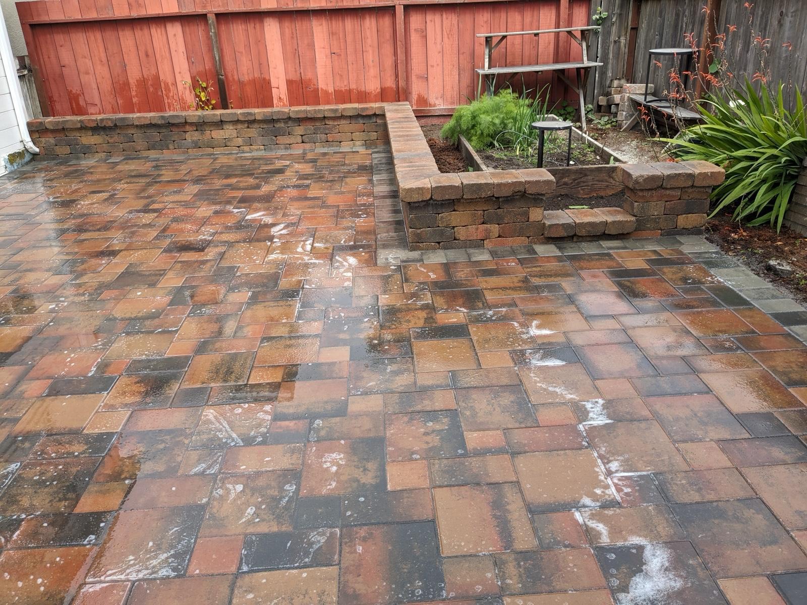 Wide view of a multi-tone paver patio with raised planters and garden beds