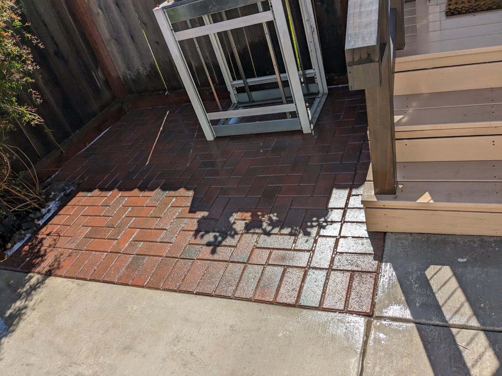 Red brick paver landing in a herringbone pattern beside composite deck steps and a wood fence