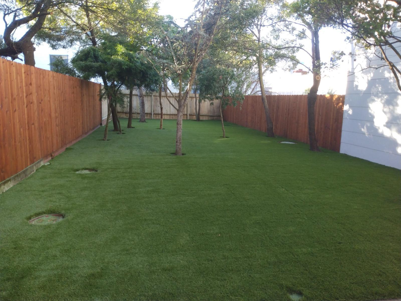 Artificial turf backyard with mature trees and new wood fencing