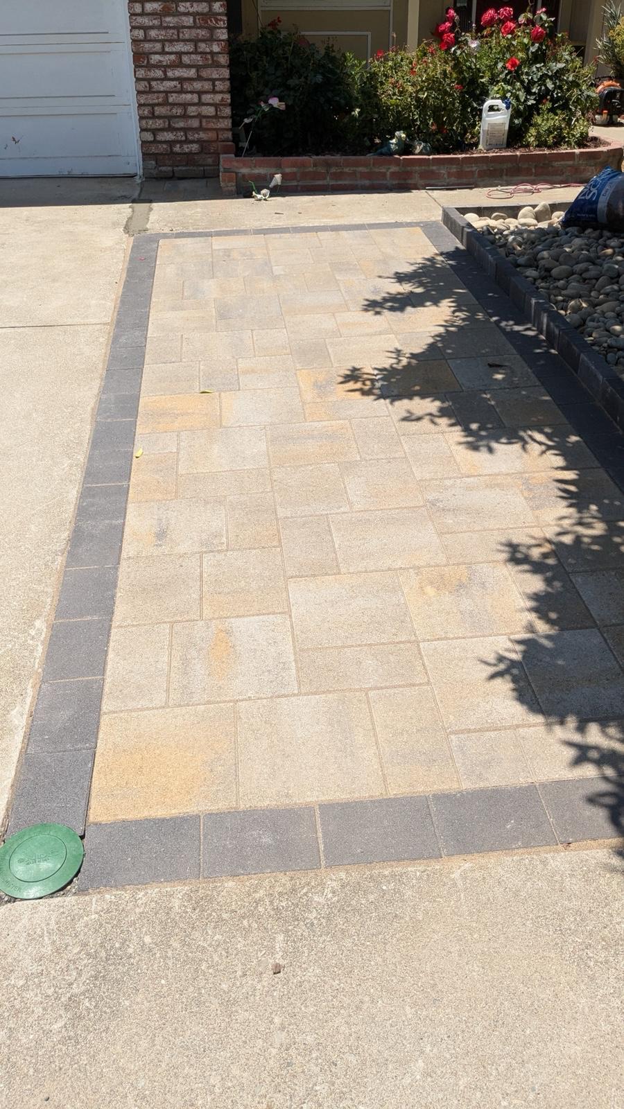 Beige paver walkway with charcoal border next to a river-rock bed